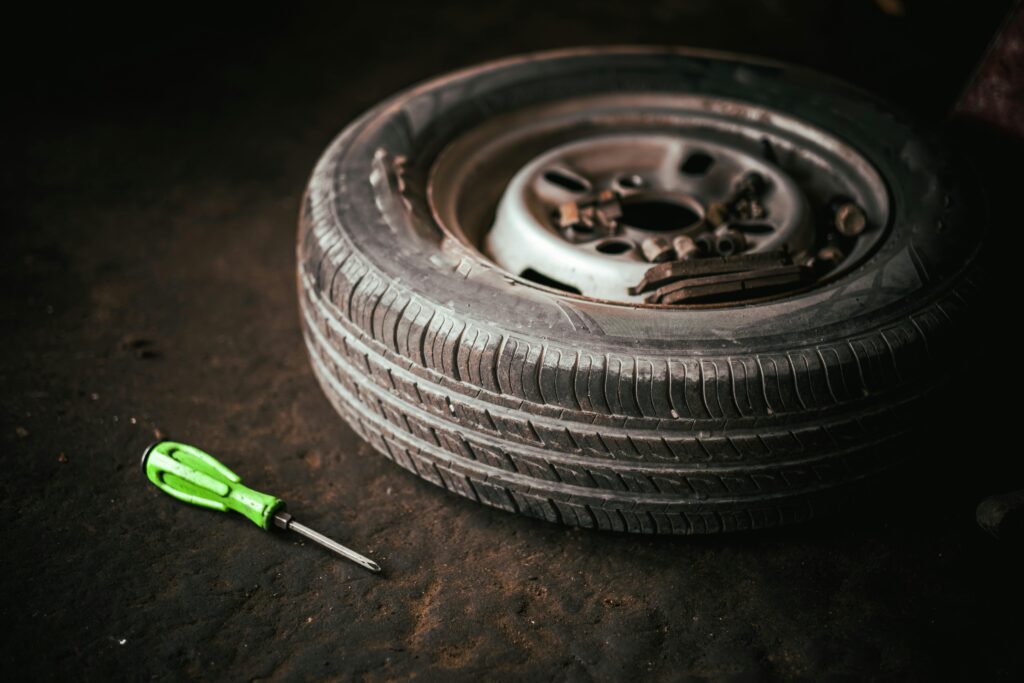 A car tire and green screwdriver placed on the garage floor, representing automotive repair.